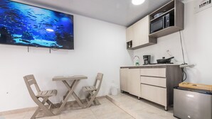 Una cucina compatta con un tavolo da pranzo e sedie, un forno a microonde, un piccolo frigorifero e un grande acquario a parete.
