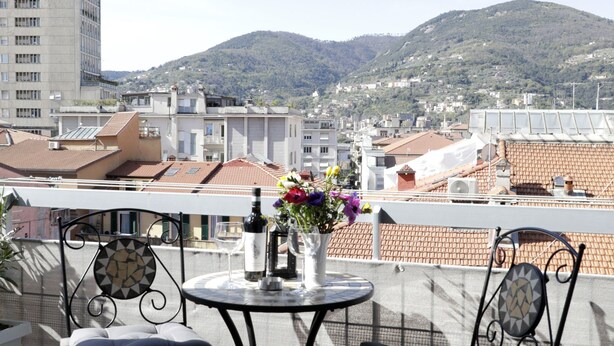 Ein Balkon mit zwei Stühlen und einem Tisch, mit Blick auf eine Stadtlandschaft aus Gebäuden und Hügeln.