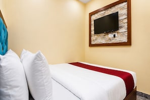 A hotel room with a bed, white pillows, a red bedspread, a television mounted on a stone wall, and a wooden frame. - Fabhotel Aai Om Residency (Mumbai)