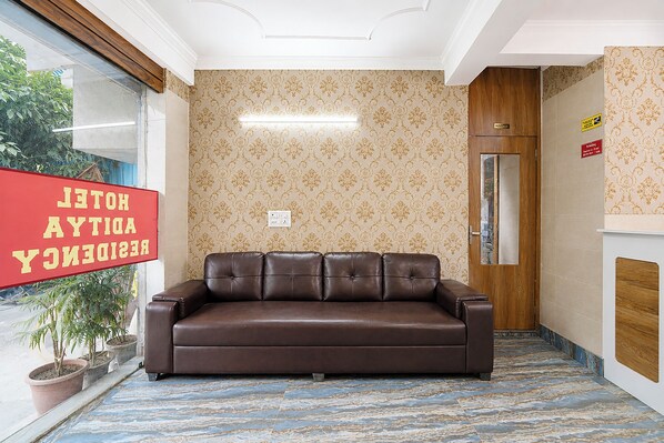 Uma área de recepção com sofá de couro marrom, papel de parede estampado, uma porta de madeira e uma placa vermelha.