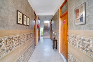 Um corredor com impressões botânicas emolduradas, uma escadaria e uma parede de azulejos com padrões geométricos.