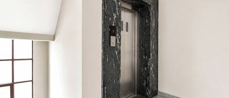 A modern elevator with a digital display, a marble wall, and a patterned floor.
