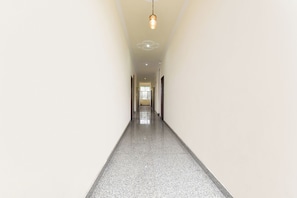 A long, narrow hallway with a polished floor, a hanging light fixture, and a door at the end. - Fabhotel Aqueens Plaza (Jaipur)