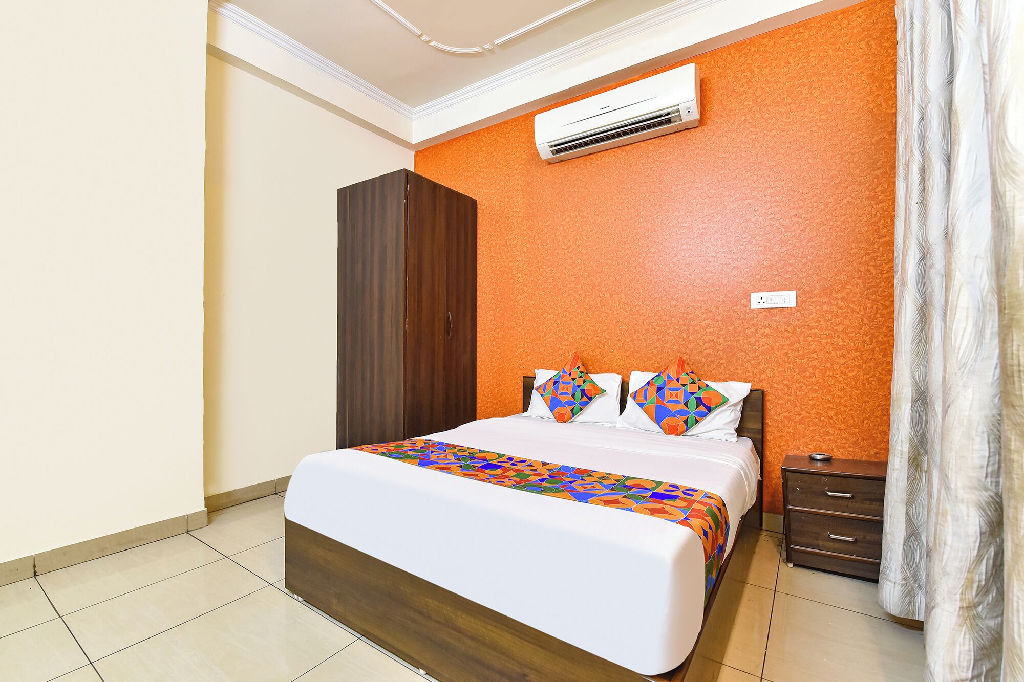 A bedroom with a bed, an air conditioner, a wardrobe, and a nightstand.
