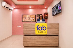 Ein Empfangstresen mit dem Logo von 'fab hotels', einem gerahmten Bild von Pferden, einer Klimaanlage und einer wandmontierten Anzeige.