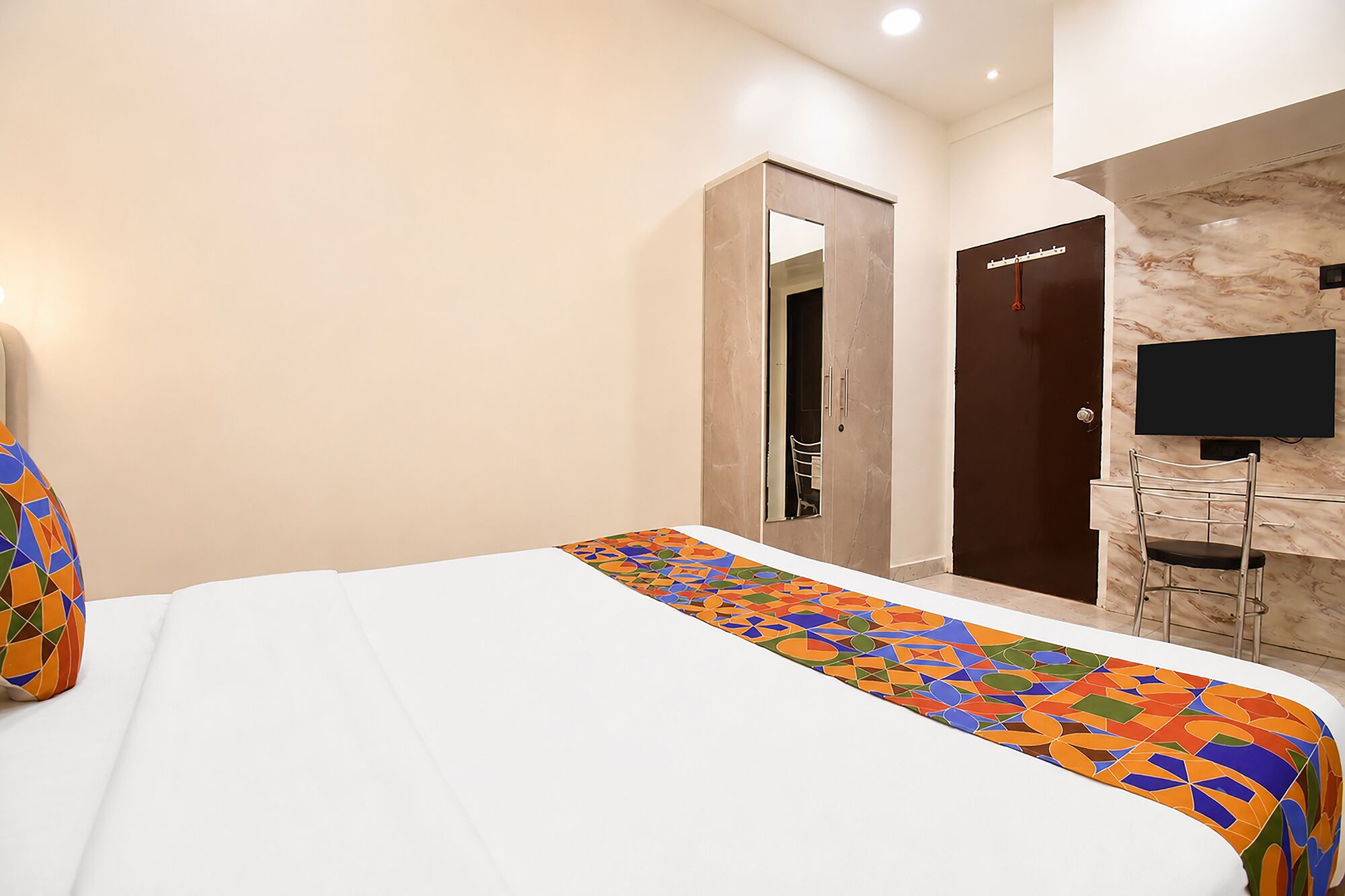 Quarto de hotel com cama, escrivaninha com cadeira, televisão e porta.