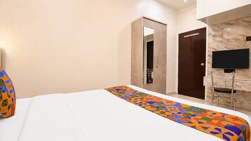 Quarto de hotel com cama, escrivaninha com cadeira, televisão e porta.