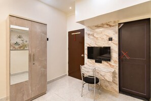 A hallway with a marble wall, a television mounted above a marble counter, a door with a red handle, and a chair. - Fabhotel Aundh Homtel (Pune)
