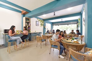 A dining area with wicker chairs and tables, a counter with a television, and a view of the outdoors. - FabHotel Aura Azure, Mahalaxmi Nagar (Indore)