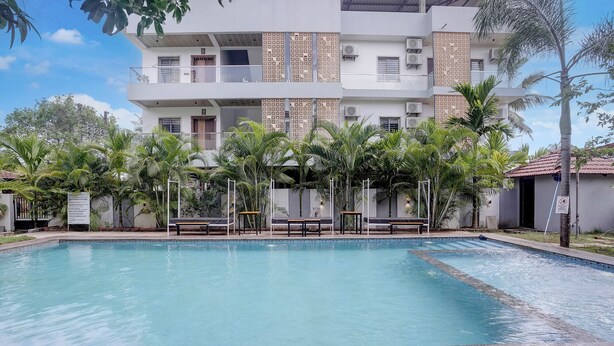 Una piscina con muelle de madera, rodeada de palmeras y un edificio de varios pisos con balcones.