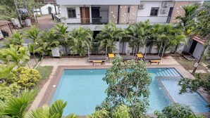 Un espace piscine comprenant deux piscines distinctes, entouré de palmiers et bordé d’un bâtiment doté d’un balcon.