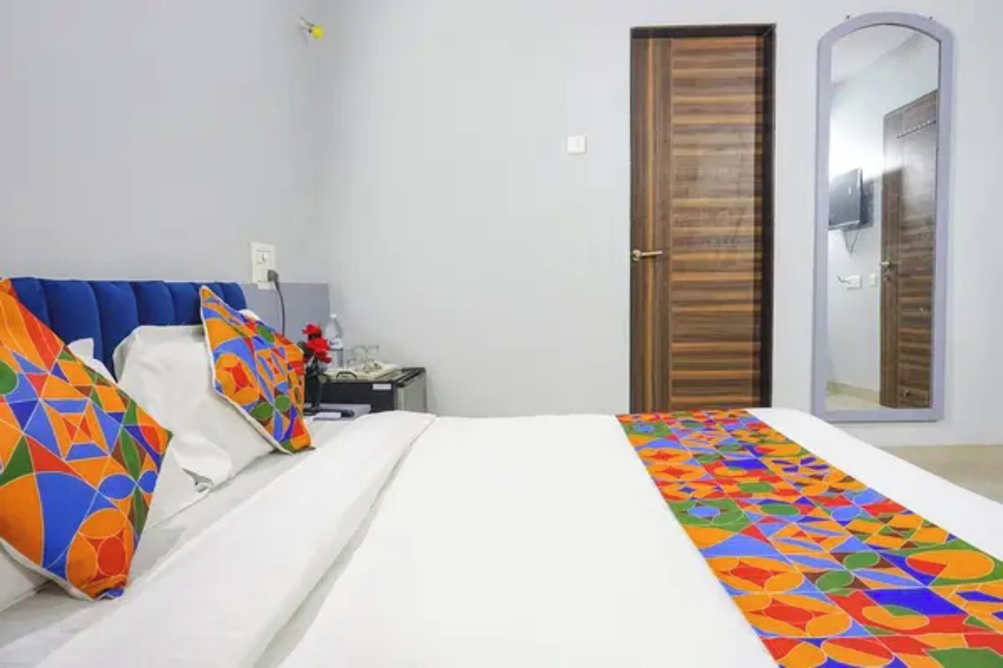 A bedroom with a bed, a nightstand, a mirror, and a door.