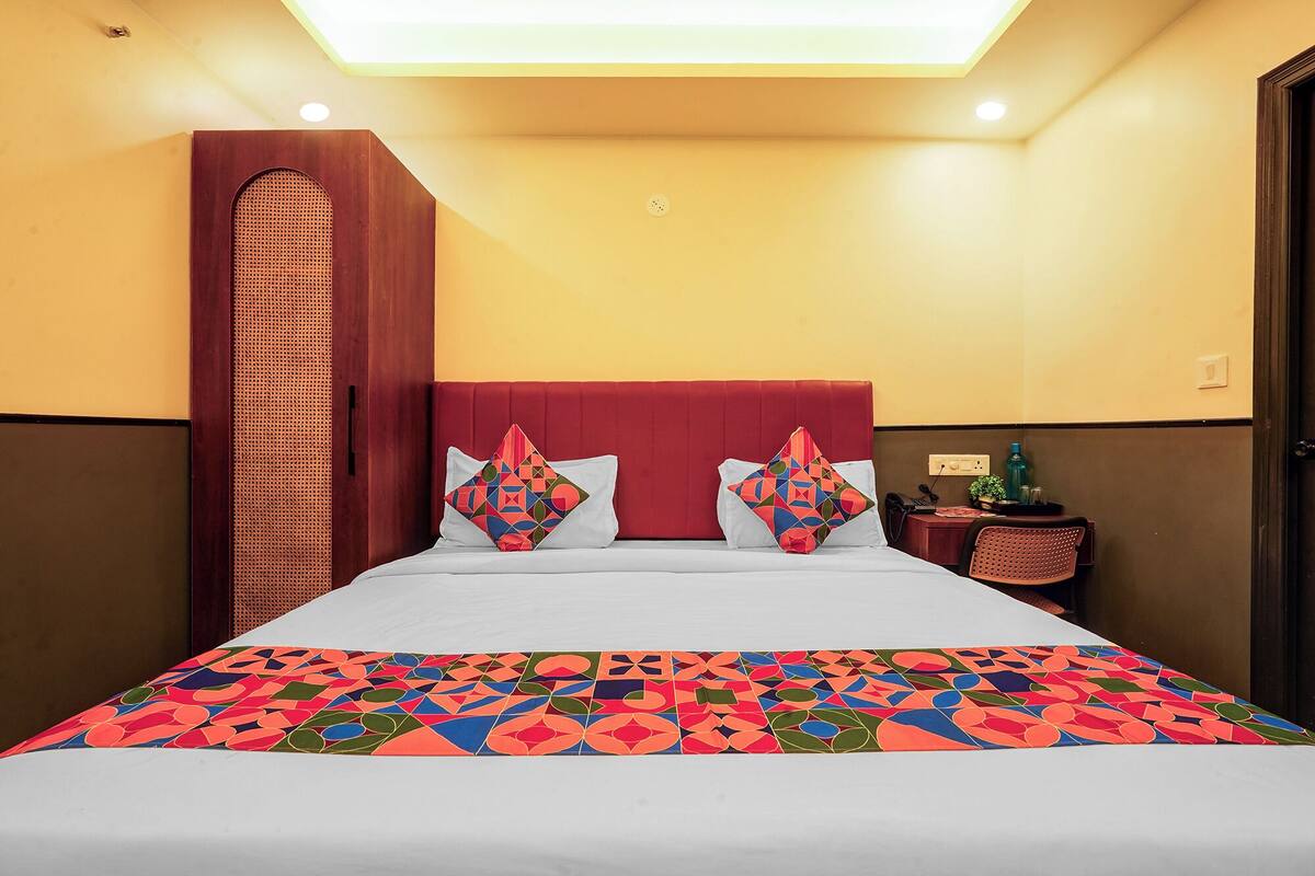A hotel room with a bed, a nightstand, a chair, and a wall-mounted shelf.