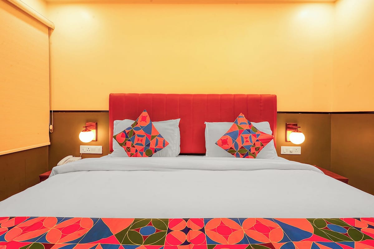 A hotel room with a bed, two pillows, bedside lamps, and a wall-mounted light.