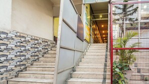 Eine Treppe mit Steinstufen führt zu einer Tür mit rotem Gitter, eine Wand mit Steinmusterung, und ein gelbes Schild über der Tür.