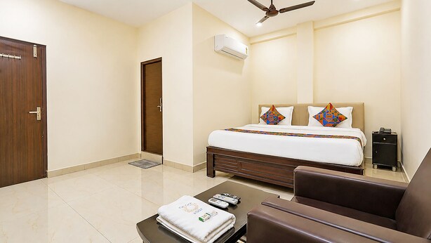 Habitación de hotel con cama, ventilador de techo, equipo de aire acondicionado, escritorio con silla y mesita de noche.