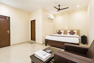 Ein Hotelzimmer mit Bett, Deckenventilator, Klimaanlage, Schreibtisch mit Stuhl und Nachttisch.