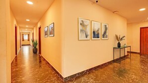 Un pasillo de hotel con suelo de mármol, obras de arte enmarcadas y una planta en maceta.