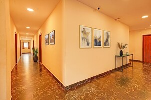 Ein Hotelgang mit Marmorböden, gerahmten Kunstwerken und einem Blumentopf.