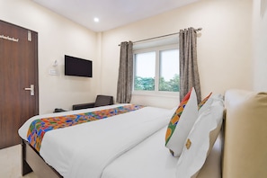 Una habitación de hotel con cama, escritorio, silla, televisión y ventana con cortinas.