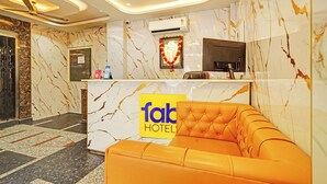 Zona de recepción de un hotel con un muro de mármol, un mostrador de recepción, un sofá y un ventilador de techo.