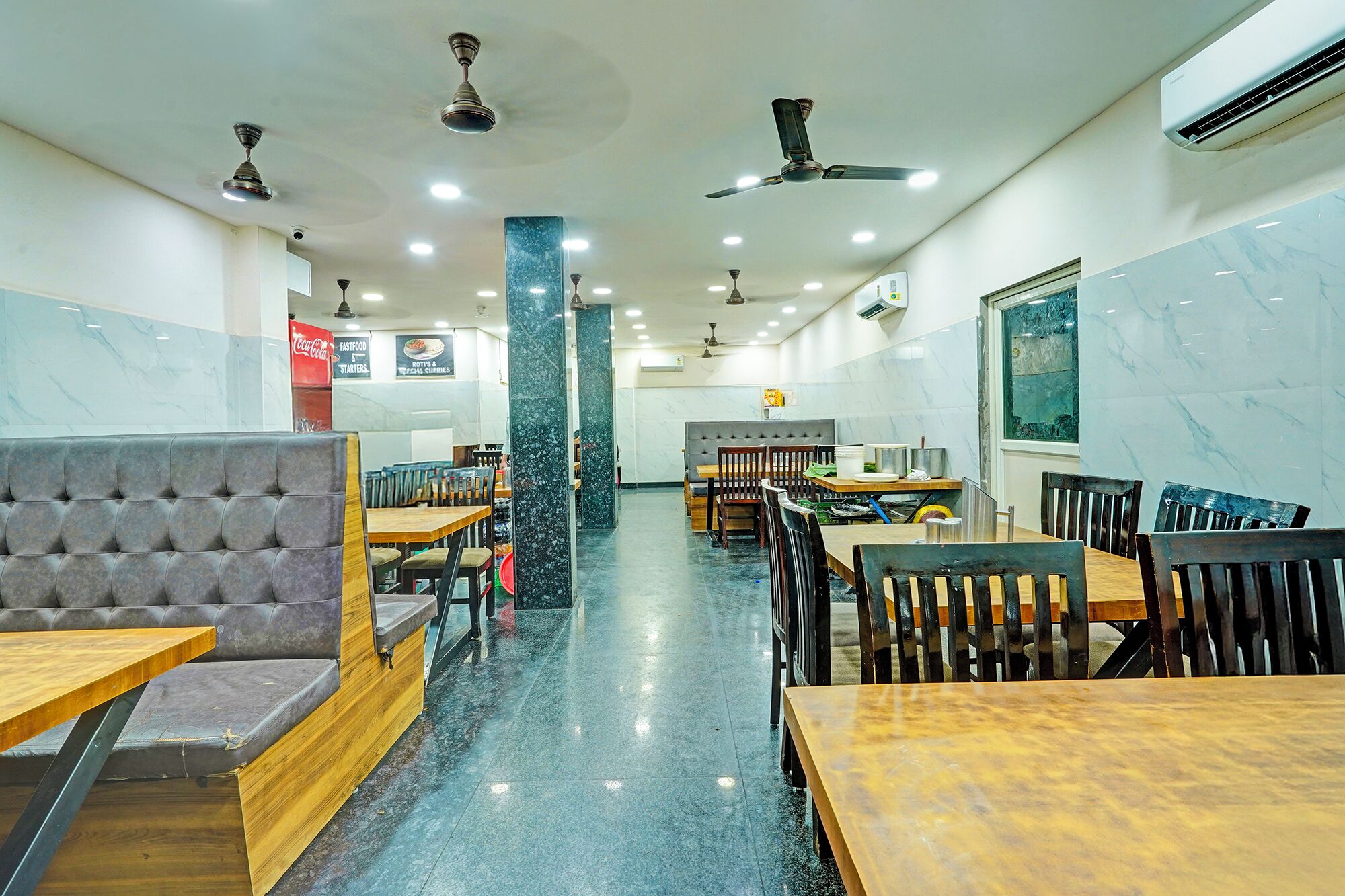 A restaurant interior with marble walls, multiple ceiling fans, and a variety of seating arrangements including booths and tables.