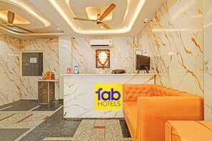 Zona de recepción de un hotel con pared de mármol, mostrador de recepción, sofá y ventilador de techo.