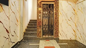 Un pasillo con suelo de mármol y una escalera que conduce a una puerta con reja de metal.