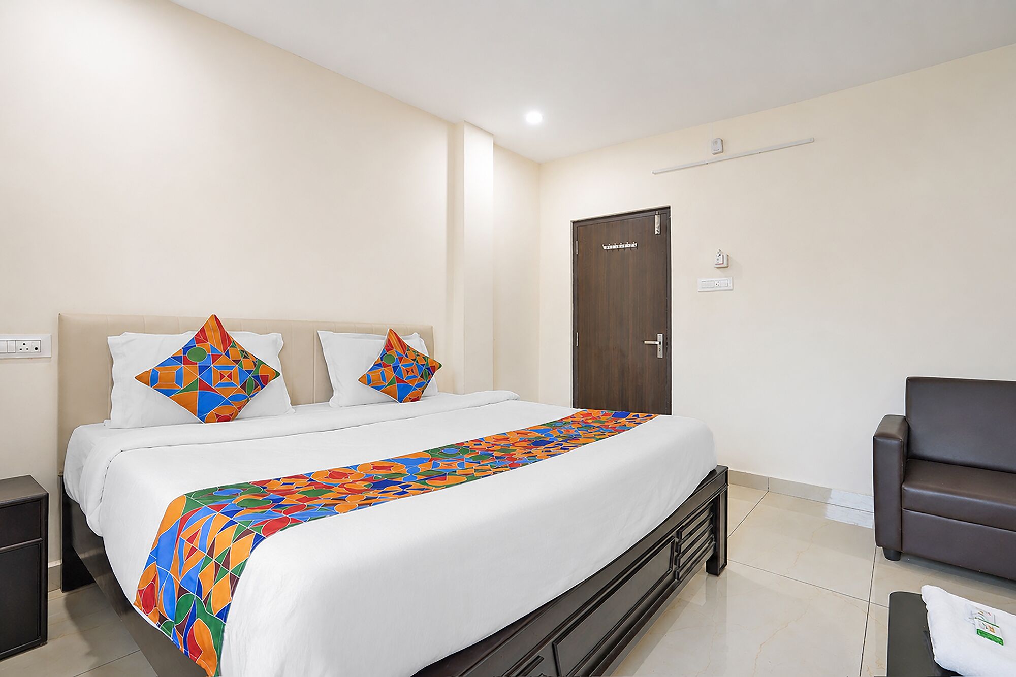 Habitación de hotel con cama, una silla, una puerta y un enchufe.