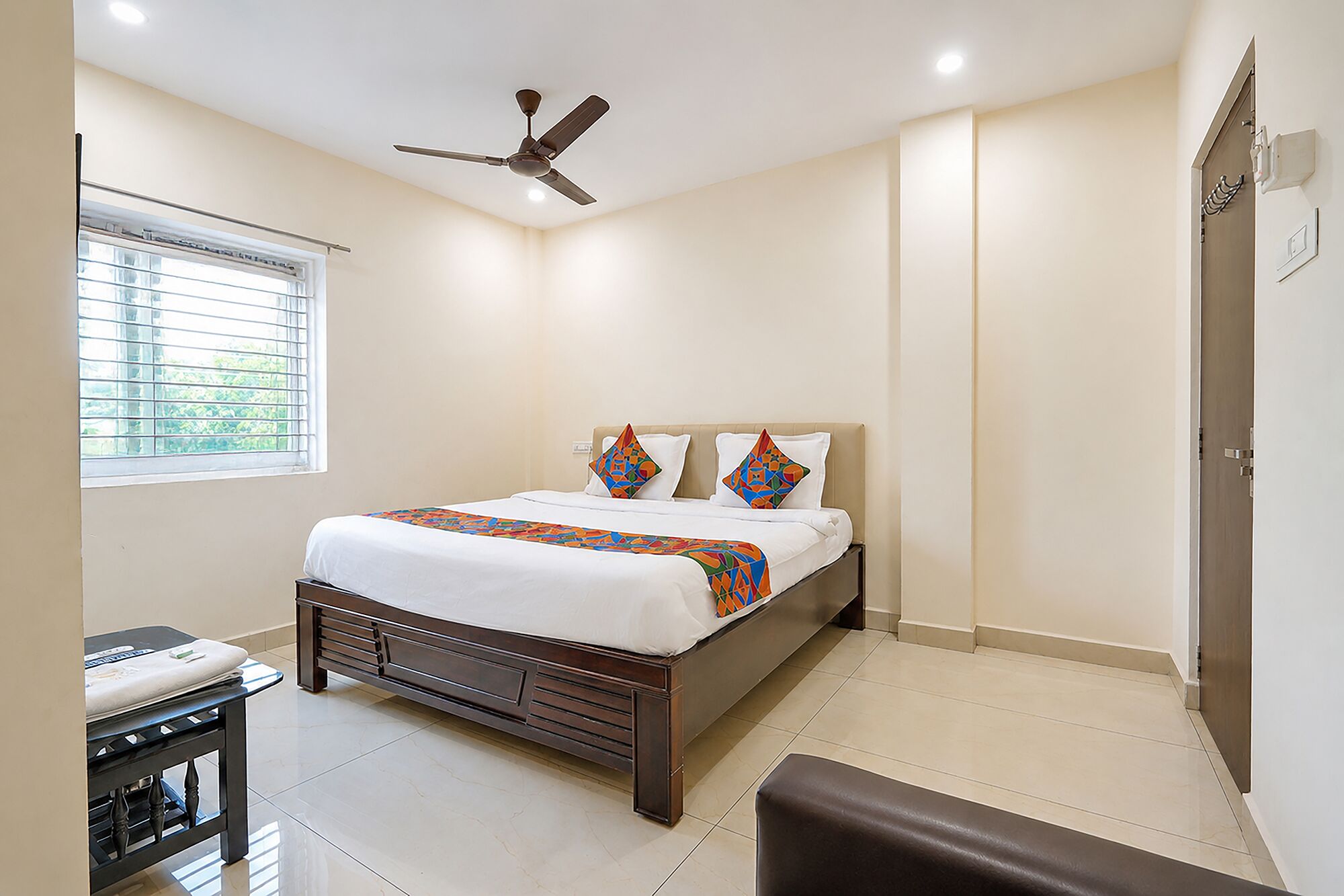 Quarto com cama, ventilador de teto, janela com persianas e porta.