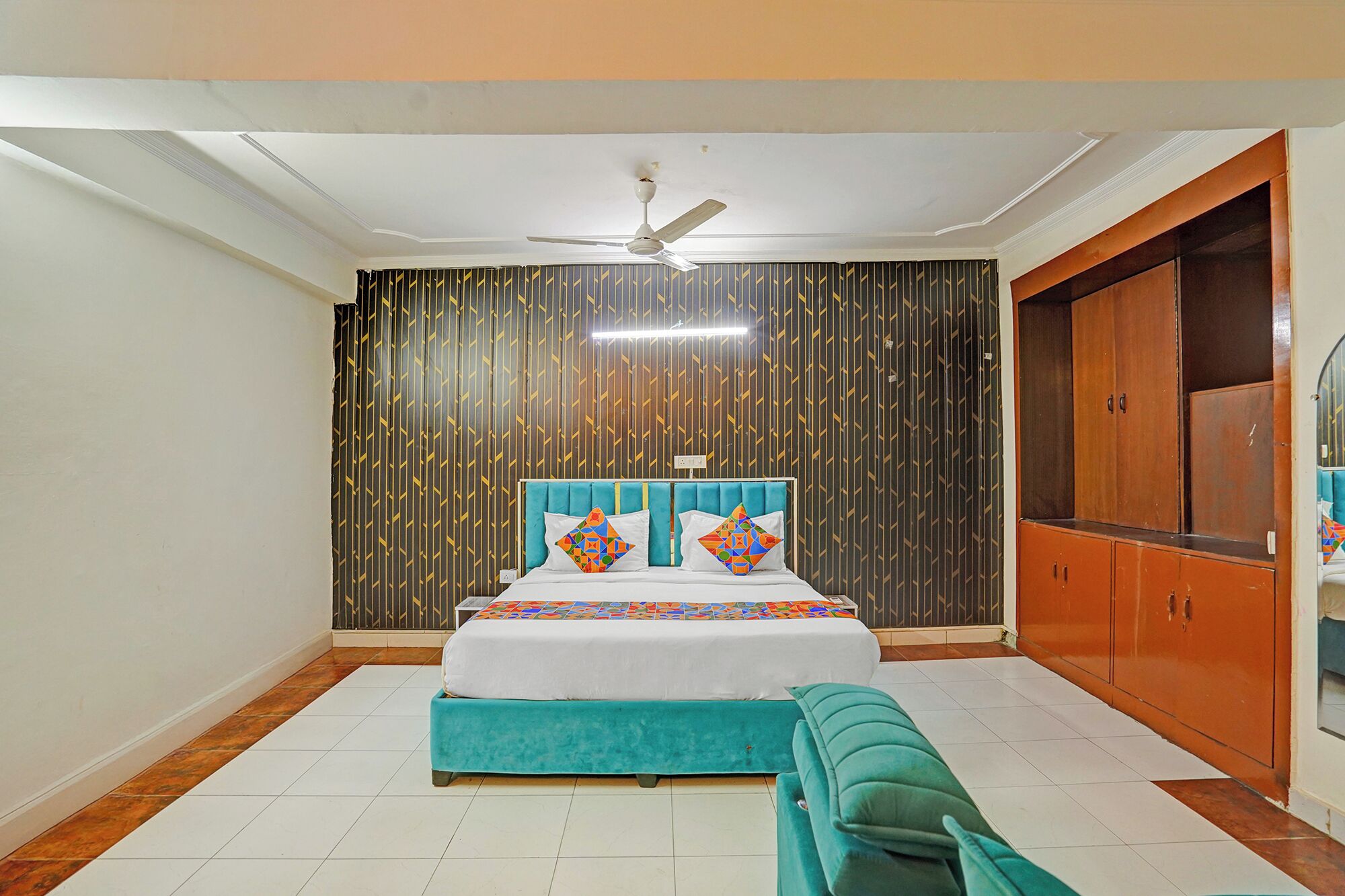 Quarto com cama, ventoinha no teto, guarda-roupa e um banquinho.