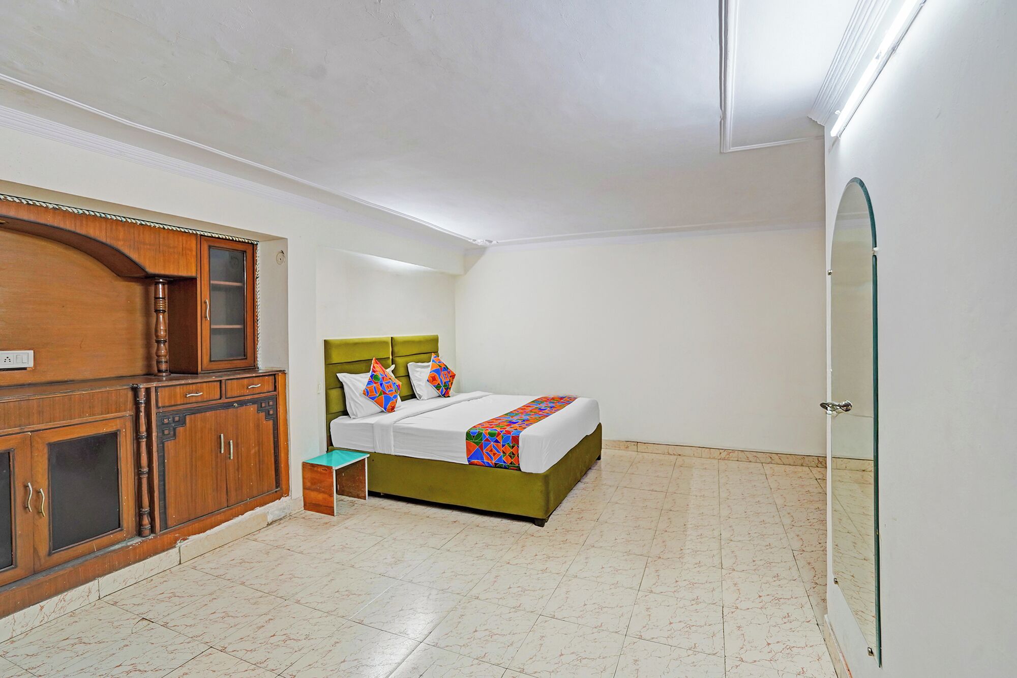 A bedroom with a bed, a wooden cabinet, a small stool, and a glass door.