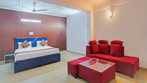 Quarto de hotel com cama, sofá vermelho, mesa de centro de vidro e ventilador de teto.