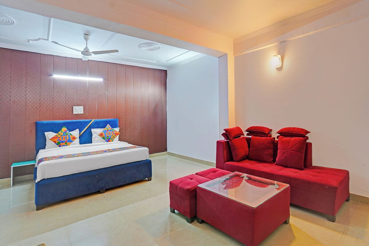 A hotel room with a bed, a red sofa set, a glass coffee table, and a ceiling fan.