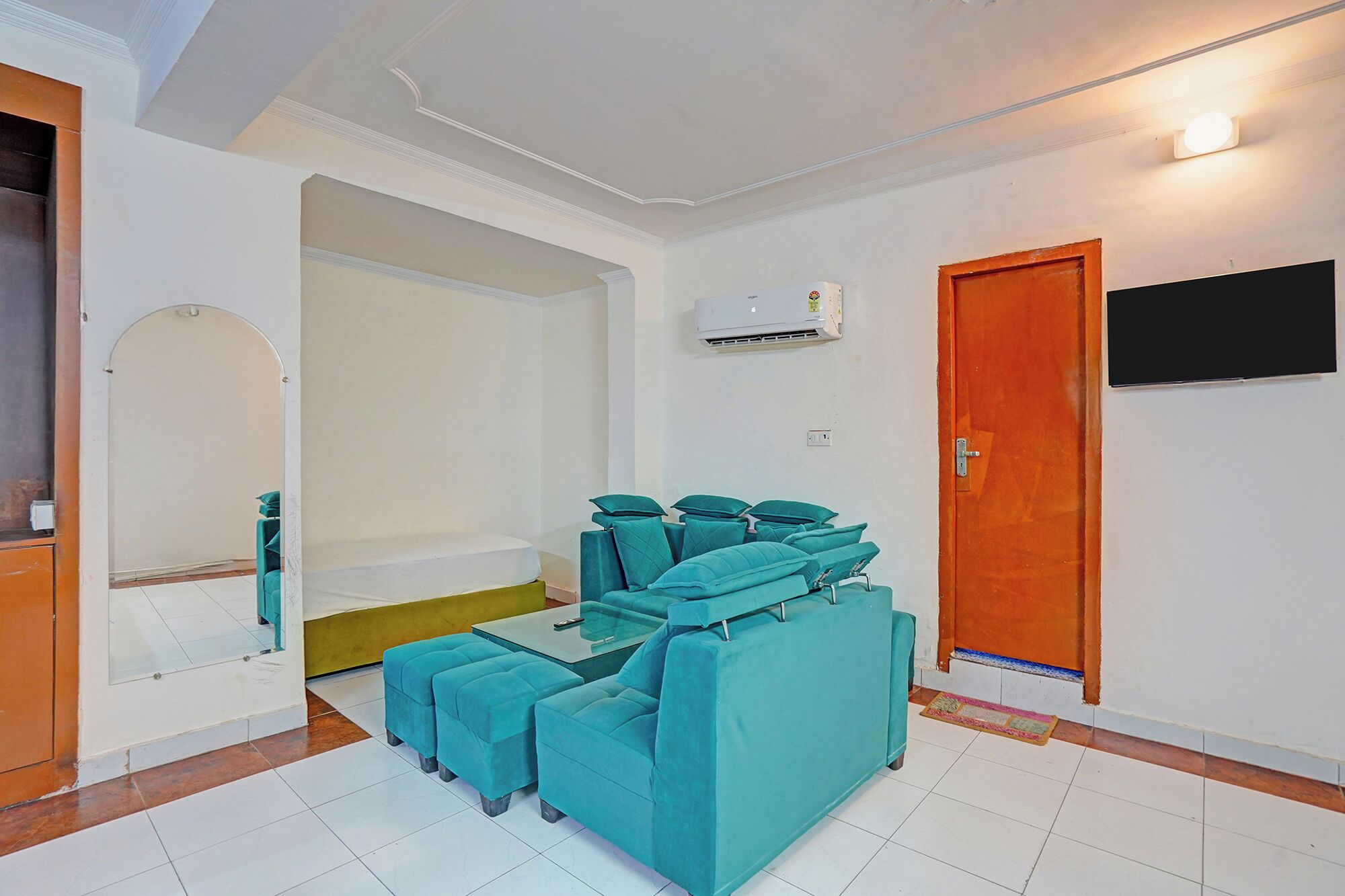 A room with teal sofas, a glass coffee table, a white tiled floor, an air conditioning unit, and a television on the wall.