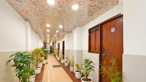 Um corredor com plantas em vasos, uma porta de madeira com um número e um teto estampado.
