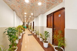 A hallway with potted plants, a wooden door with a number, and a patterned ceiling.