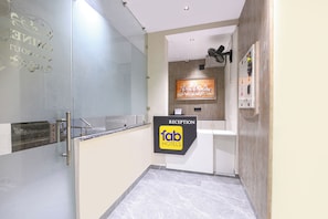 A reception area with a glass partition, a reception desk, a wall-mounted air conditioning unit, and a painting of horses. - FabHotel Eminence Grand (New Delhi)