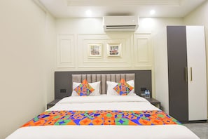 A hotel room with a bed, a wardrobe, an air conditioning unit, and framed pictures on the wall.