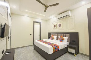 A bedroom with a bed, bedside table, nightstand, ceiling fan, air conditioning unit, and a television on the wall. - FabHotel Eminence Grand (New Delhi)
