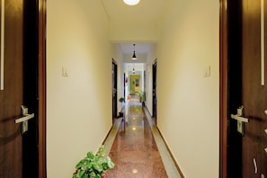 Un couloir d’hôtel avec des portes en bois, un sol en marbre poli et des plantes en pot.