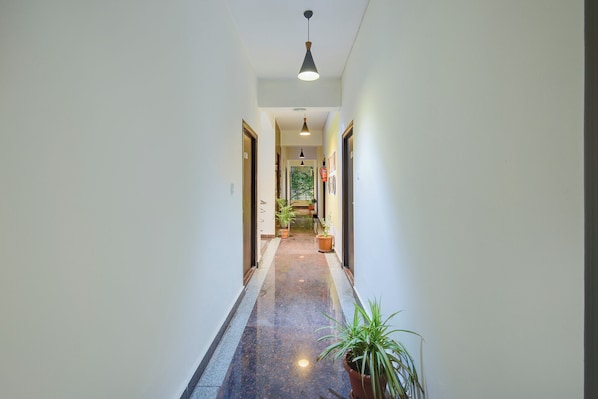 Um corredor com piso de mármore, plantas em vasos e luminária pendente.