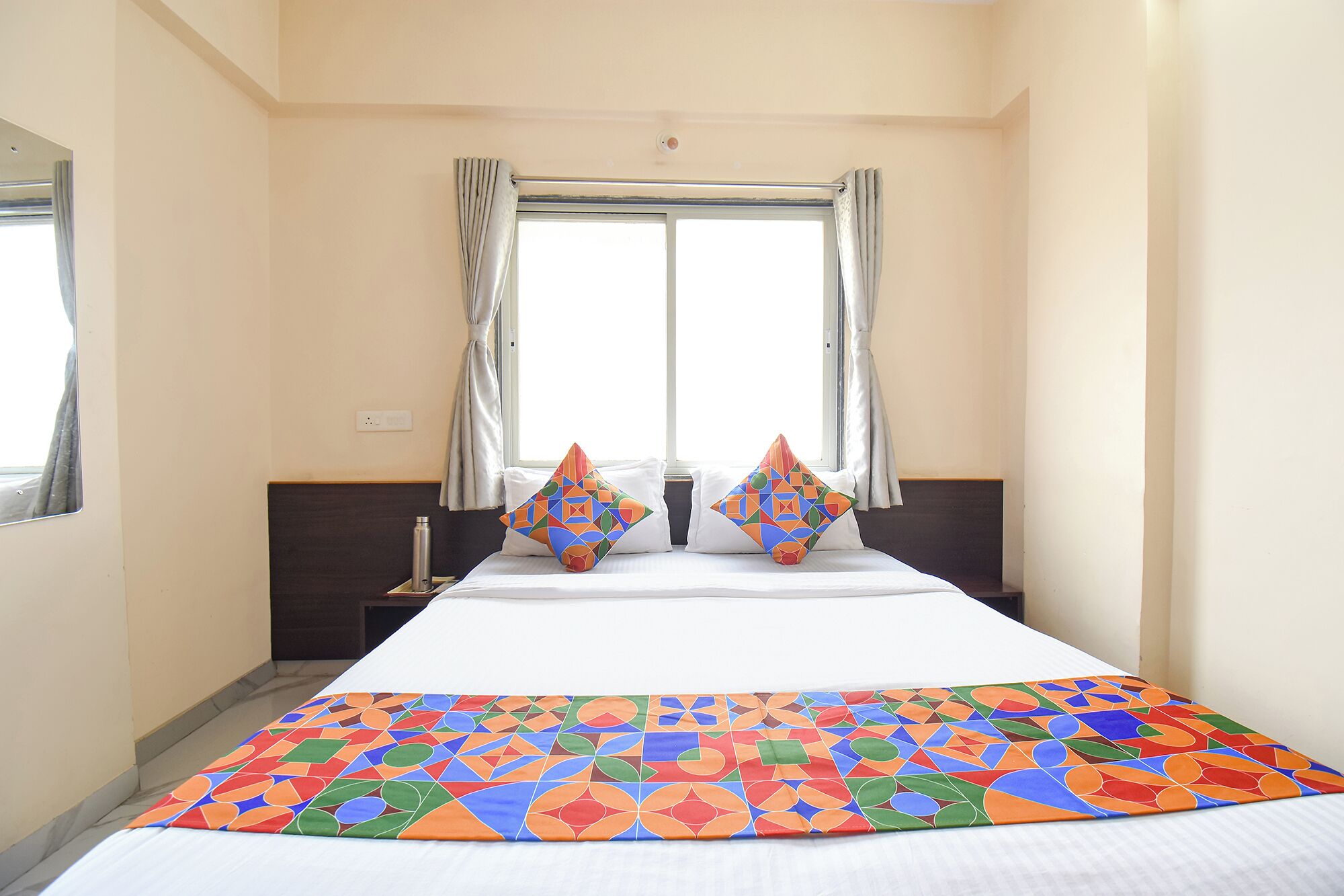 Habitación de hotel con cama, ventana con cortinas y una colcha colorida.