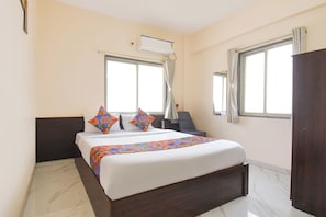 A hotel room with a bed, two windows, an air conditioning unit, a chair, and a wardrobe. - Fabhotel Himalay Guest House (Pune)