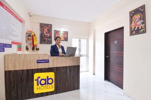 A hotel reception desk with a receptionist, a computer, and religious artwork on the walls. - Fabhotel Himalay Guest House (Pune)