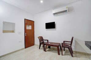 A room with a wooden door, a mounted air conditioner, a wall-mounted TV, and a small wooden table with chairs. - Fabhotel Hr Residency (New Delhi)