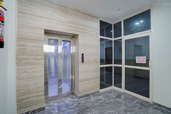 An elevator with a digital display, a glass door entrance, and a sign indicating a hotel-hospital residency. - Fabhotel Hr Residency (New Delhi)