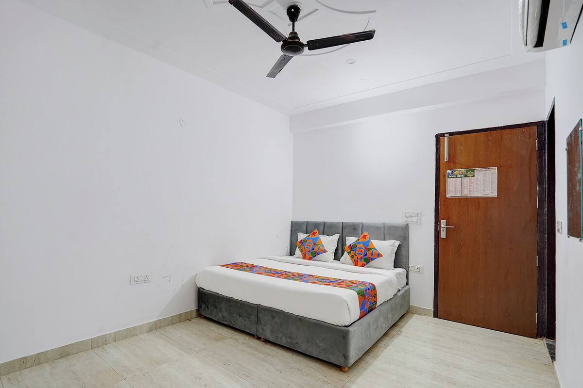 A bedroom with a bed, a ceiling fan, a door, and a wall-mounted light switch.