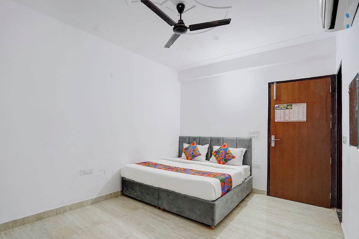 A bedroom with a bed, a ceiling fan, a door, and a wall-mounted light switch.