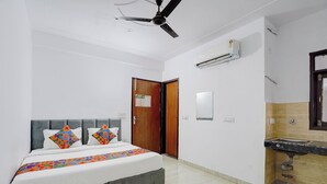 A bedroom with a bed, a ceiling fan, an air conditioning unit, a wooden door, a mirror, and a bathroom with a sink. - Fabhotel Hr Residency (New Delhi)